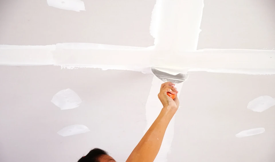 Ouvrier du bâtiment appliquant du plâtre sur les murs avec une truelle, présentant un savoir-faire artisanal dans la rénovation de la maison