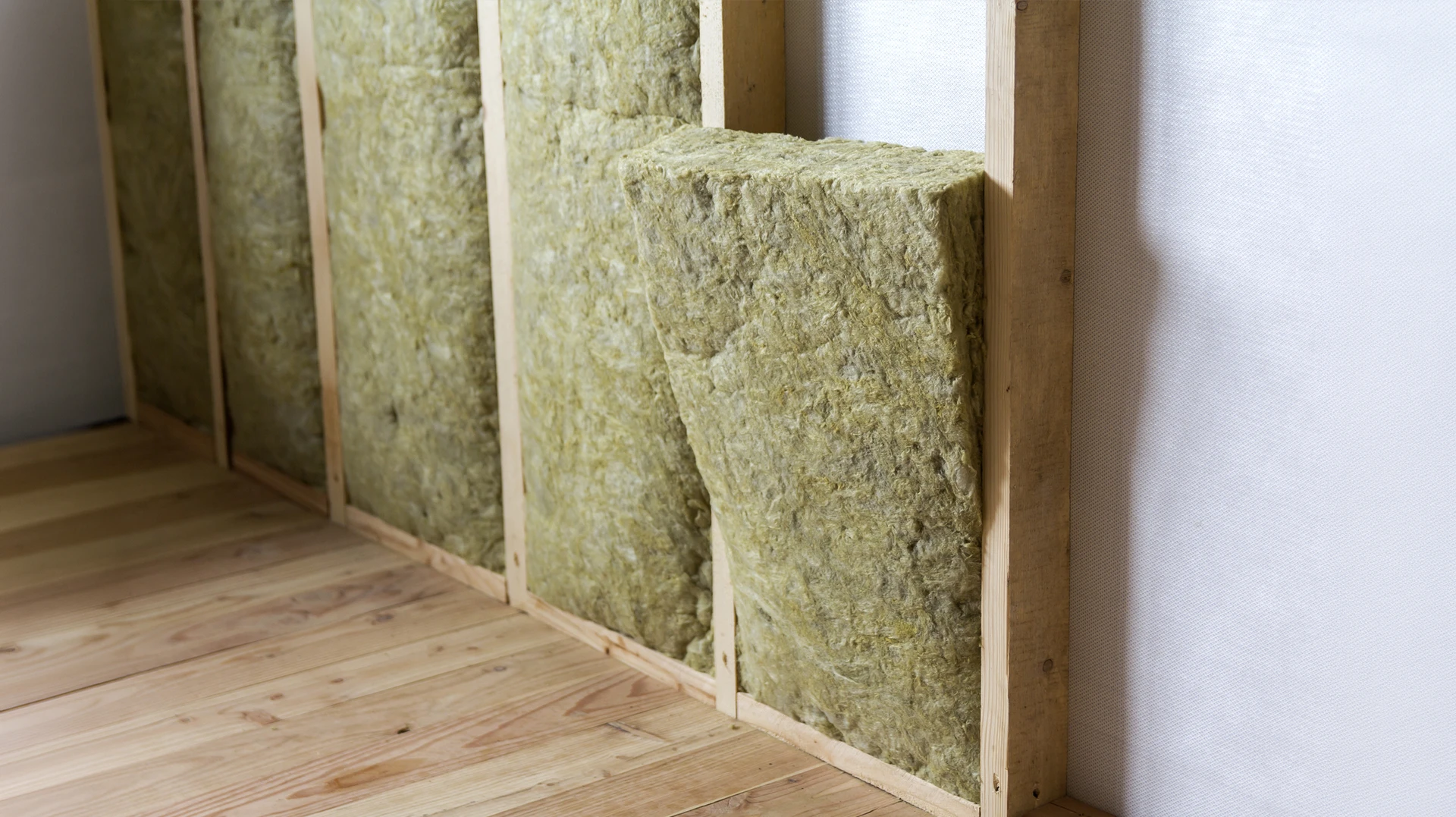 Chantier intérieur d'isolation thermique avec ouvrier installant laine de verre jaune entre montants métalliques sur mur de briques apparentes